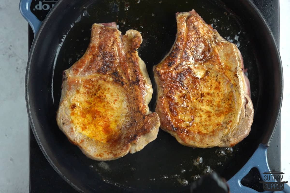 the pork chops being browned in a pan