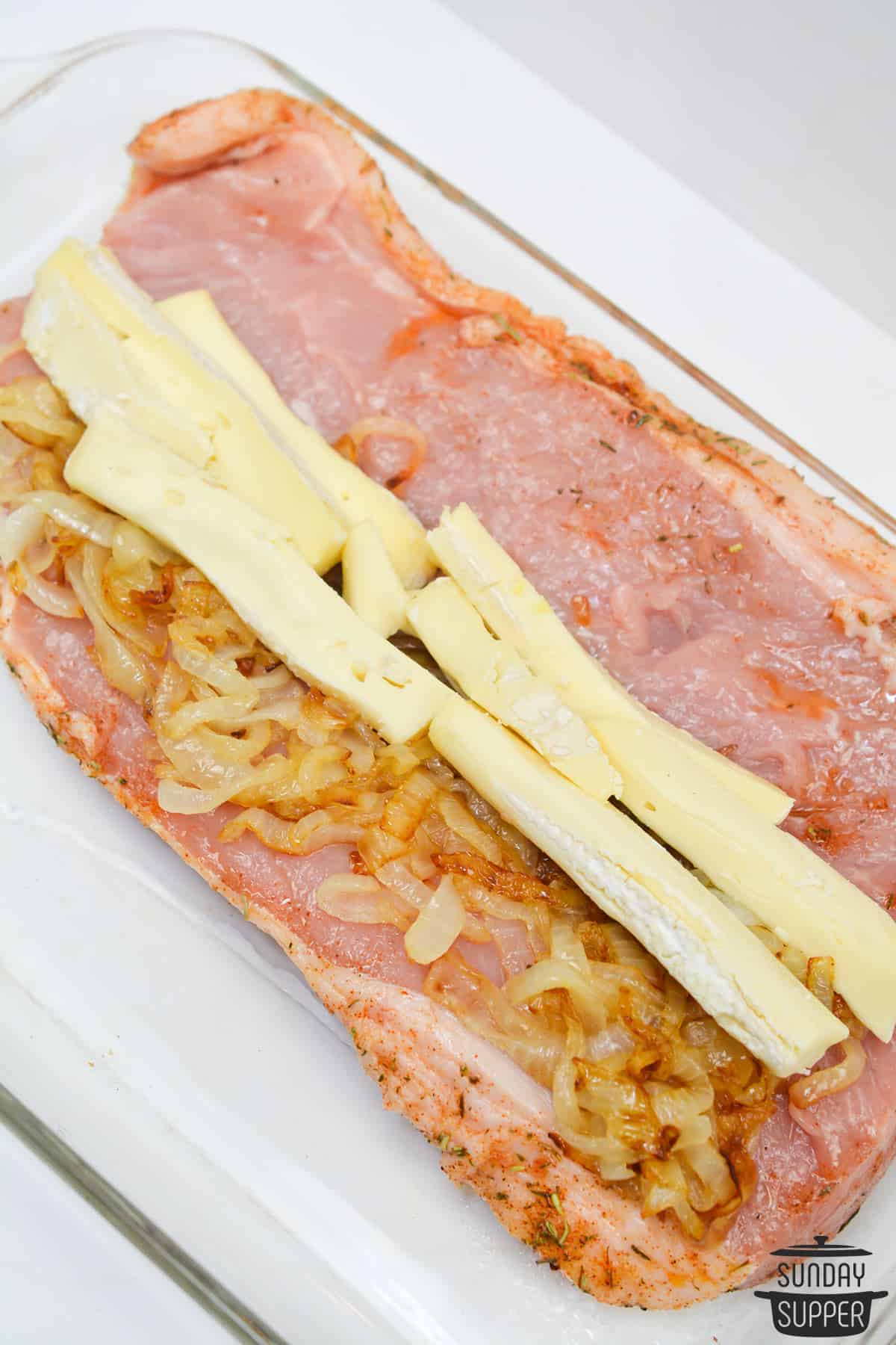 The sliced open pork tenderloin with onions and brie cheese slices layered inside