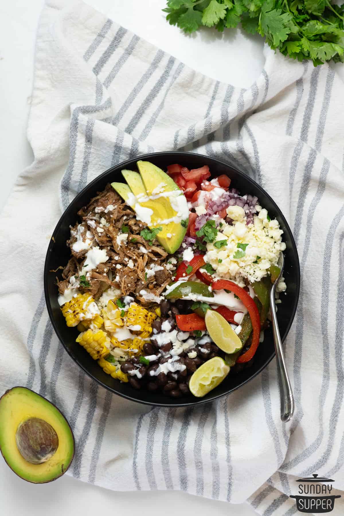 a completed carnitas burrito bowl with extra crema and lime