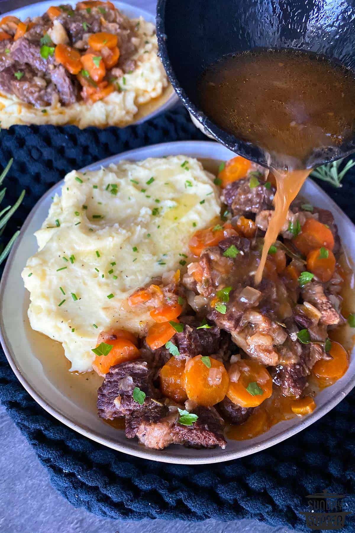 gravy being poured on a plate of short ribs and mashed potatoes