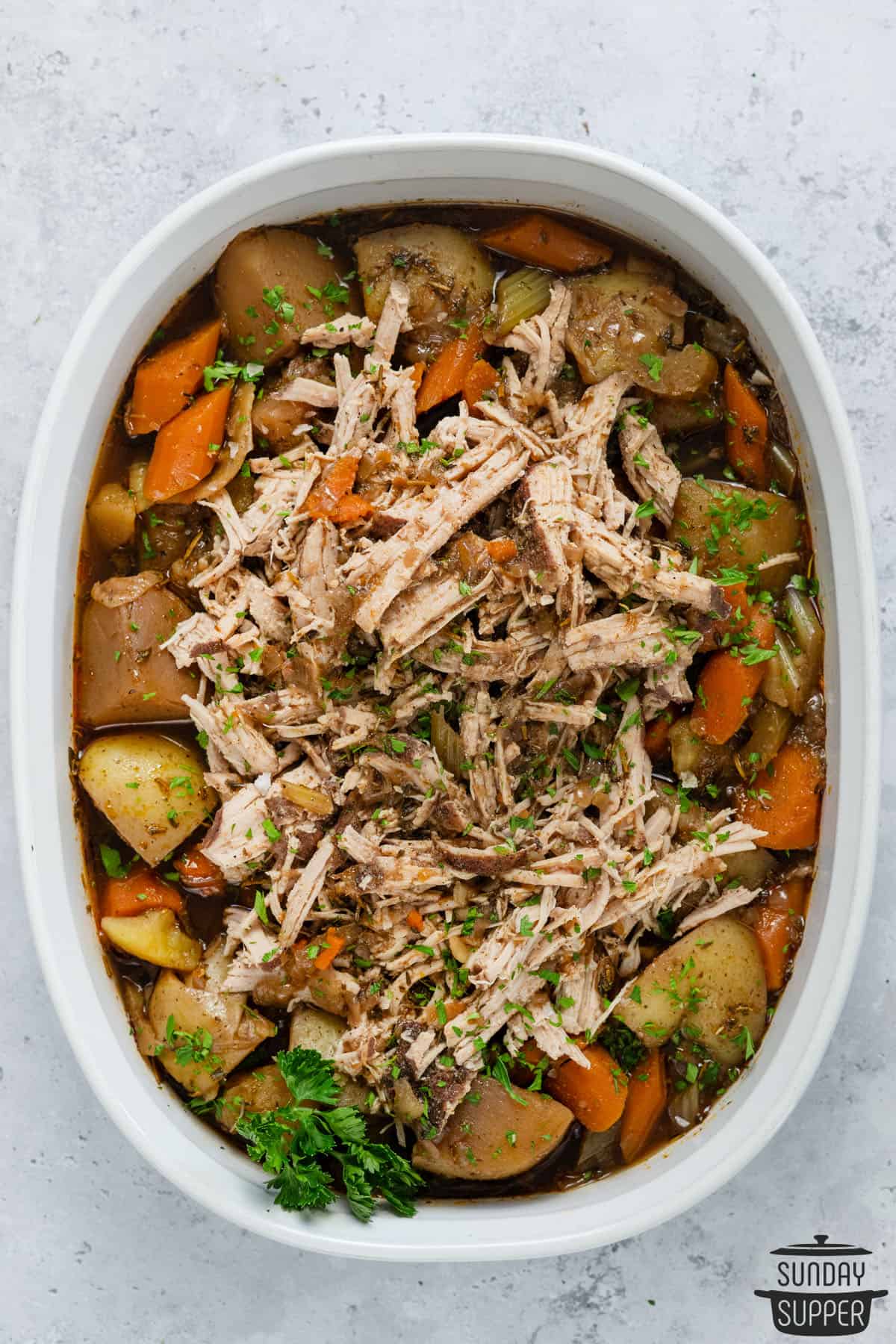 a white serving bowl filled with pork roast and veggies