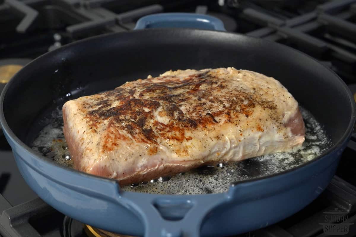 pork loin being seared in a pan with oil