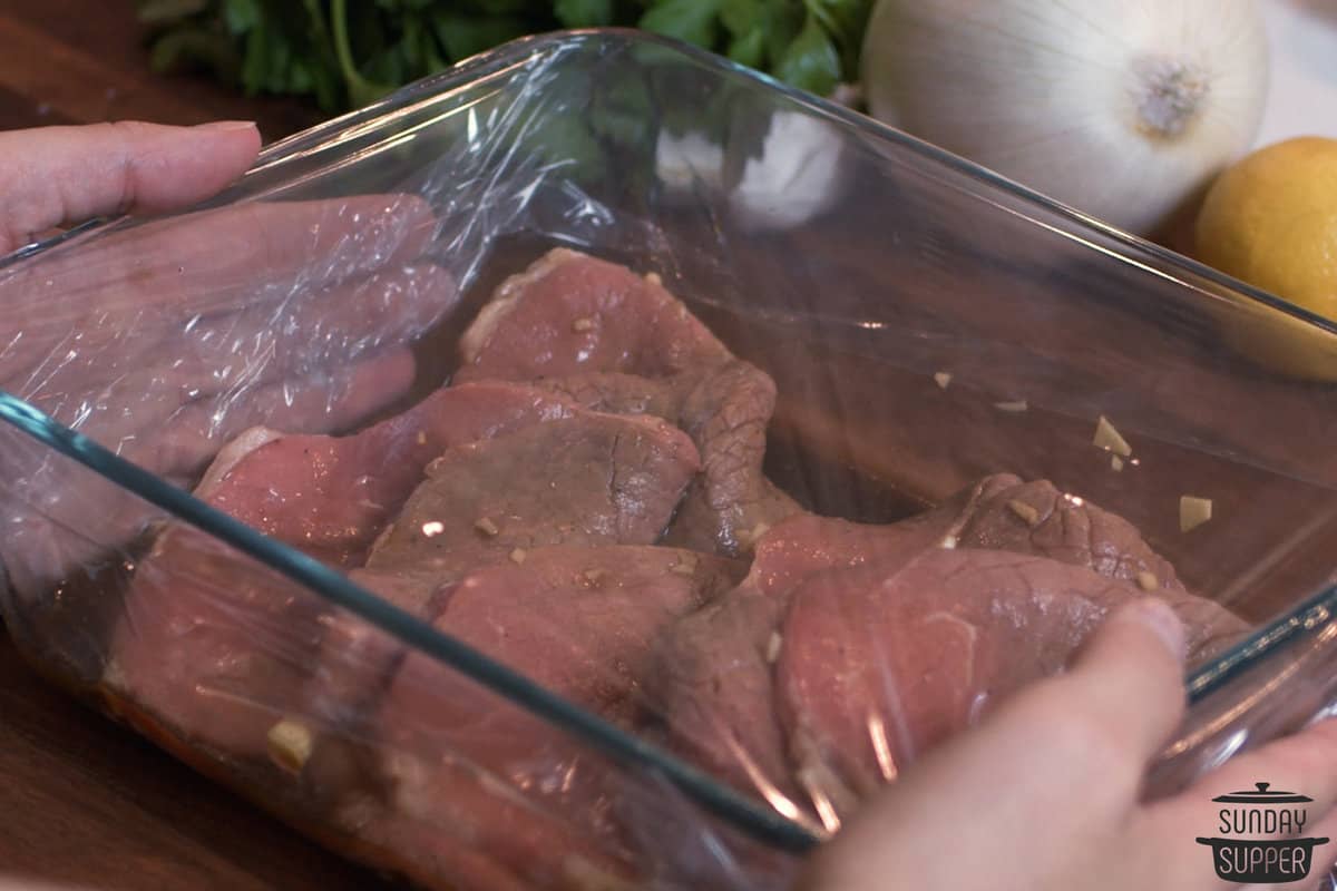the beef marinating in a dish covered in plastic
