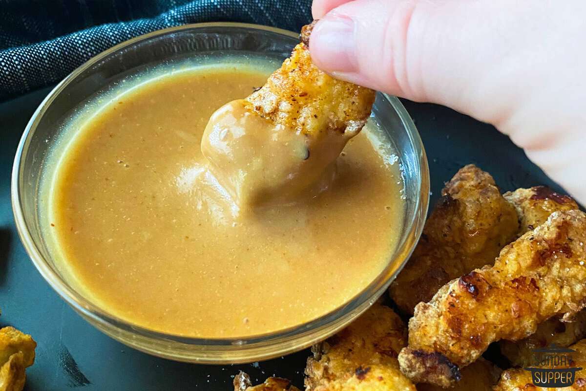 a chicken nugget being dipped into a dish of sauce