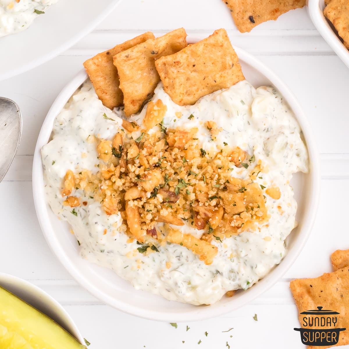 dill pickle dip topped with fried onions and breadcrumbs in a bowl with crackers