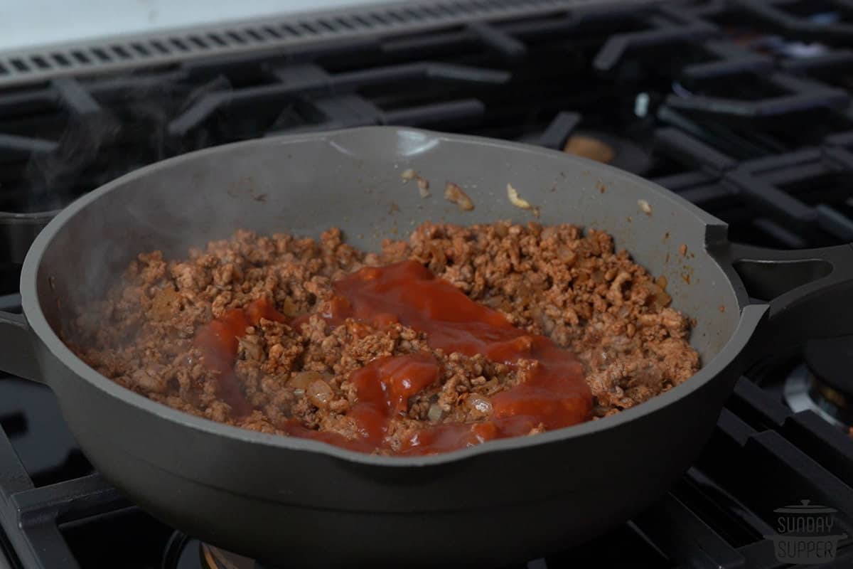 adding tomato sauce to ground pork in a skillet