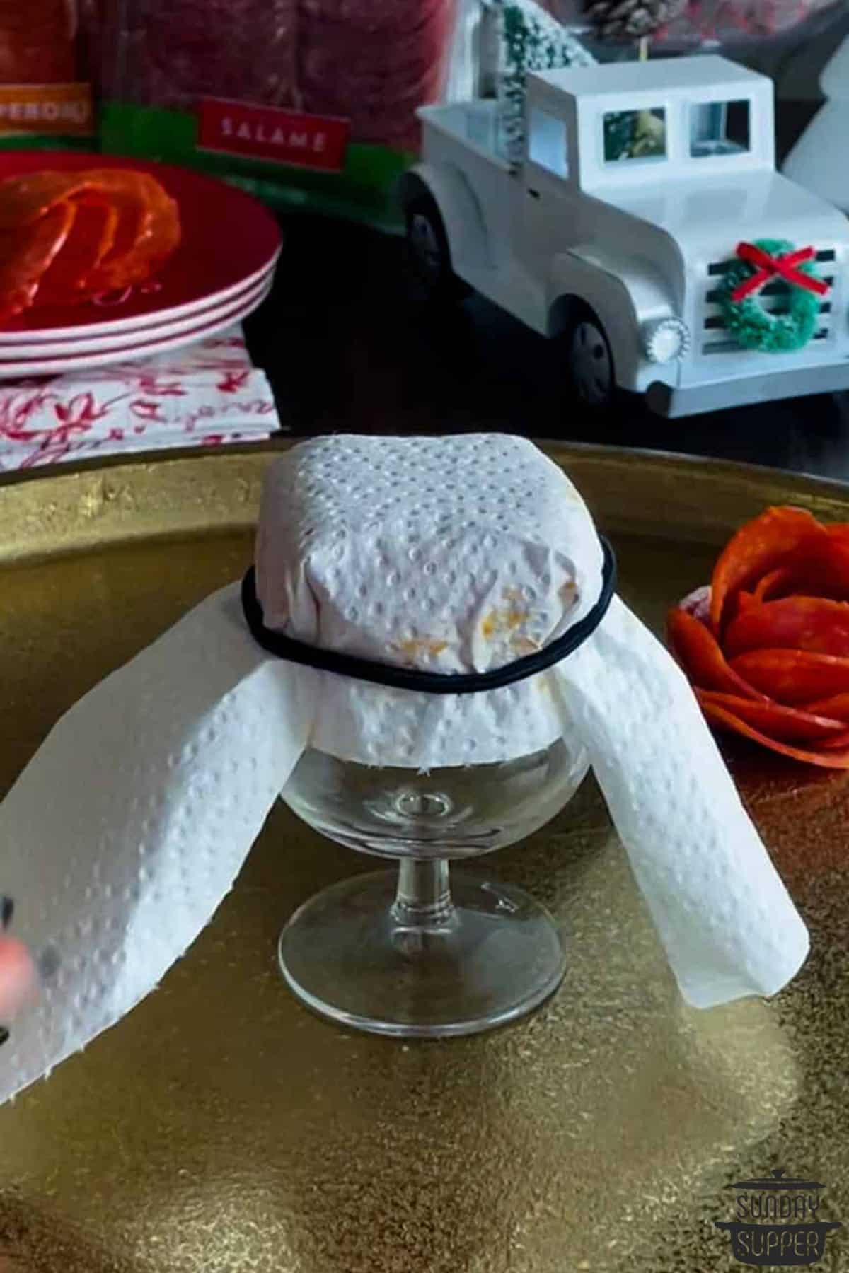 paper towel tied over a pepperoni meta flower on a glass