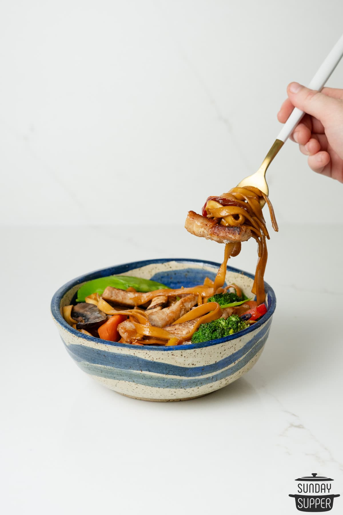 pork stir fry inside of a blue bowl with a fork full of noodles over top