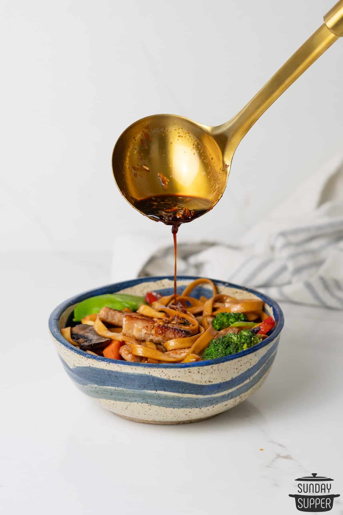 pouring teriyaki sauce over pork stir fry in a blue bowl