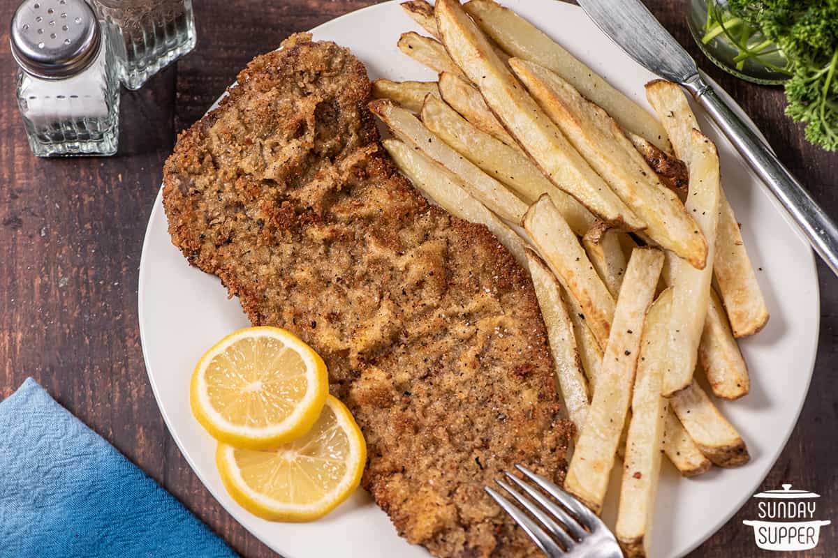 beef milanesa on a plate with fries and lemon slices