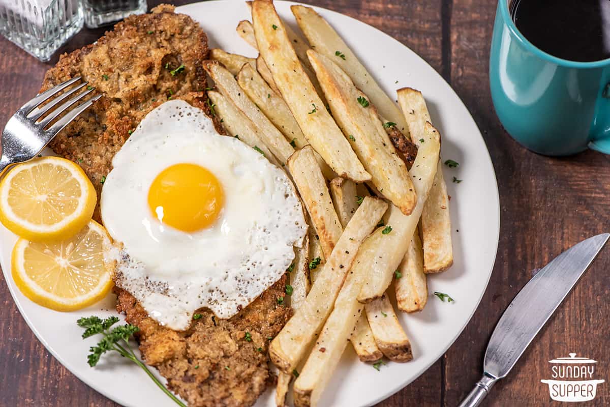 a plate with beef milanesa, fries, lemon slices, and a fried egg