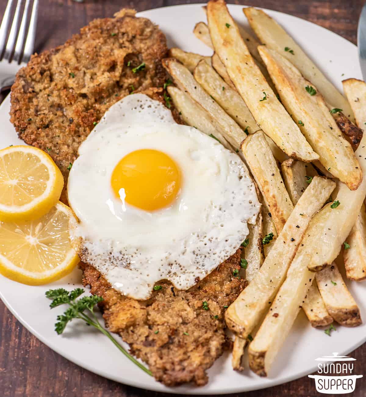 steak milanesa on a plate with fries, lemon slices, and a fried egg