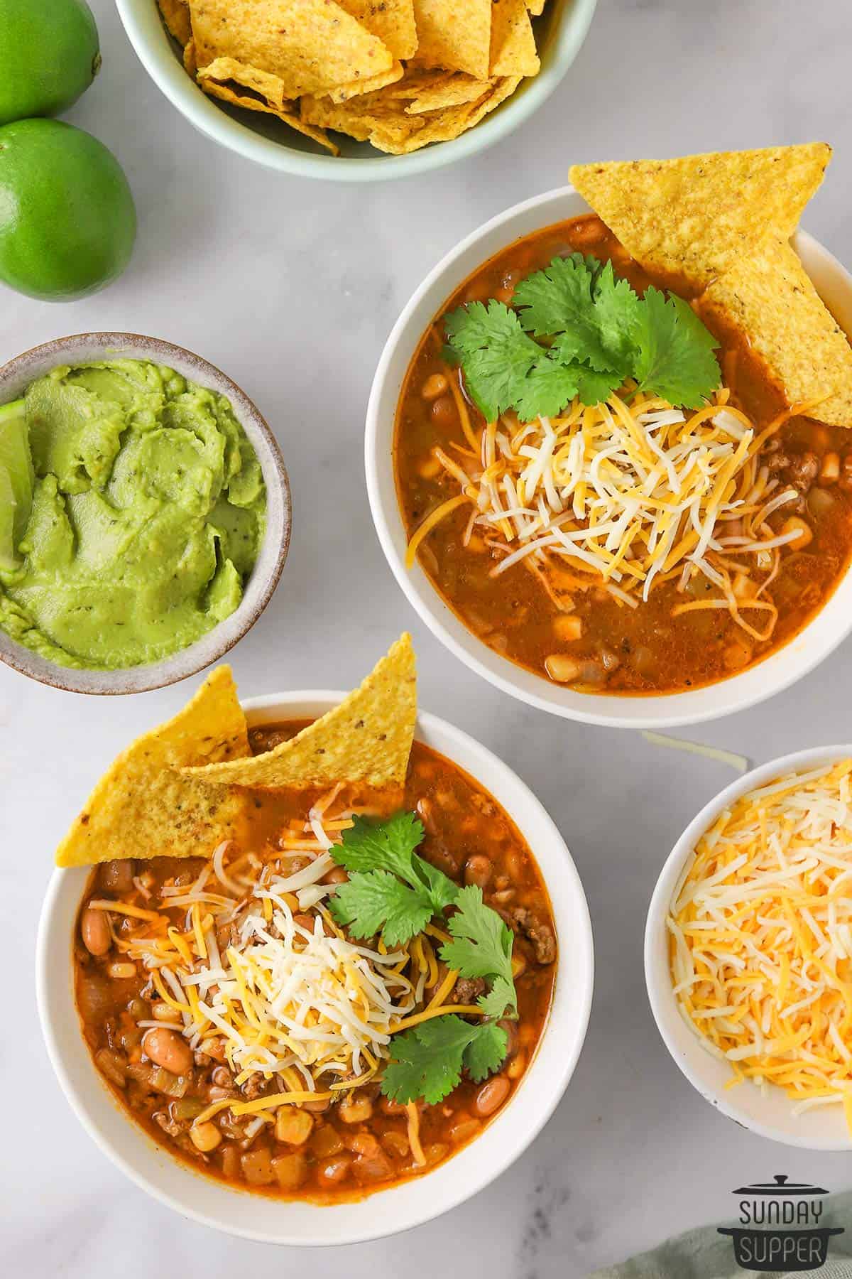 two bowls of taco soup with extra cheese, chips, and guacamole