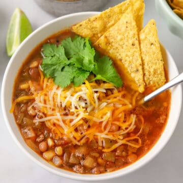 a bowl of taco soup with added cheese, cilantro, and tortilla chips