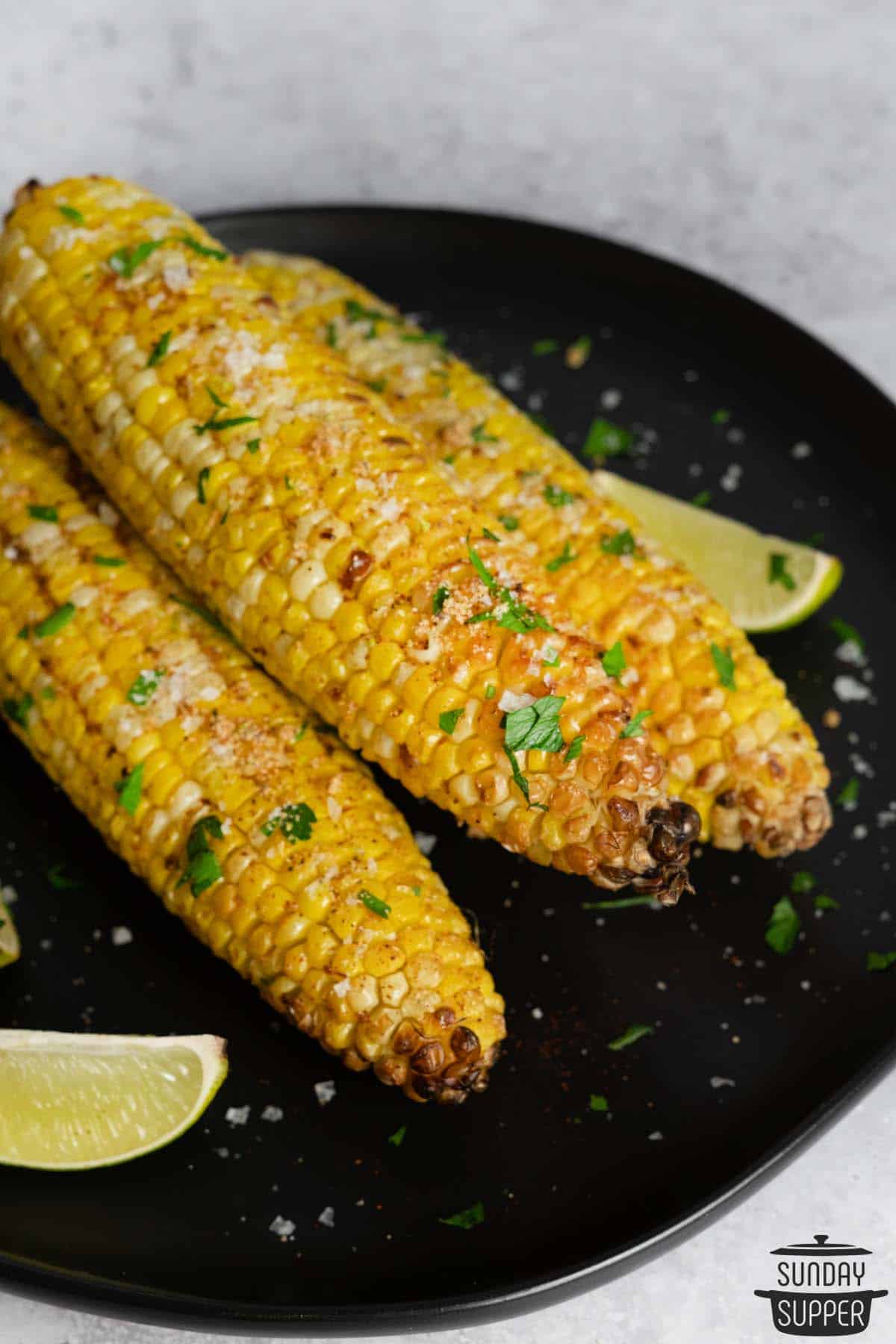 three ears of air fried corn on a plate with lime wedges