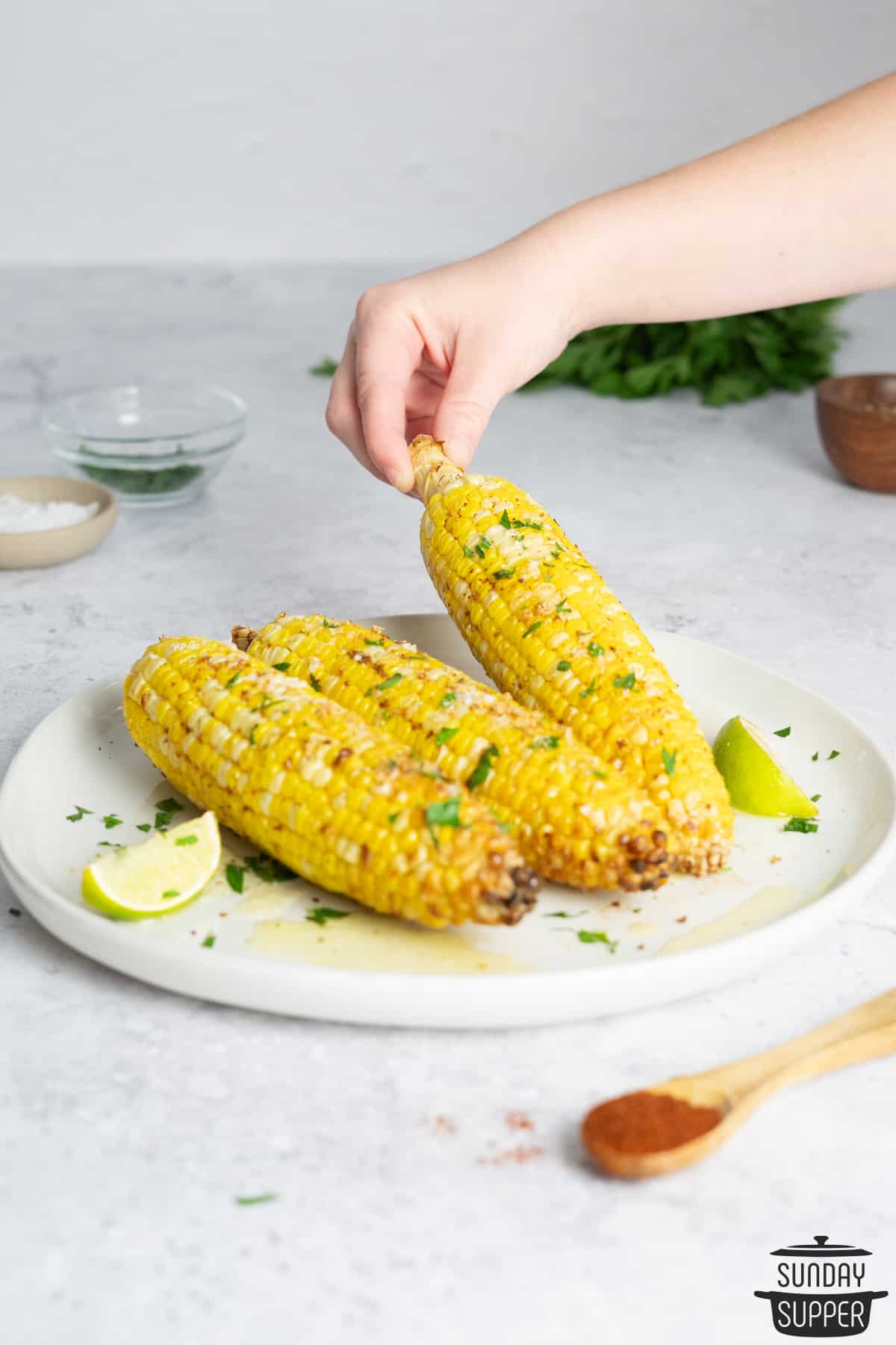 a hand picking up an ear of corn off a plate