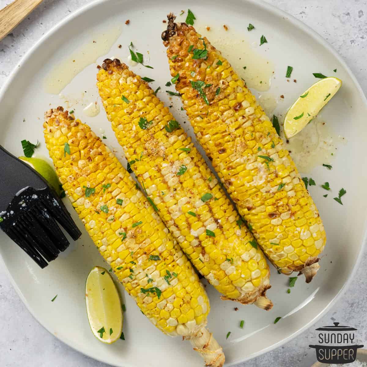 three ears of air fried corn on a white plate with lime and butter