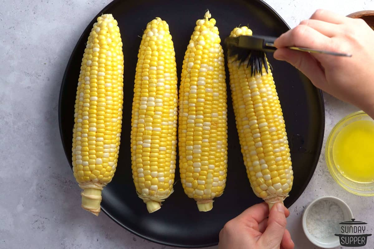 butter being brushed on shucked corn