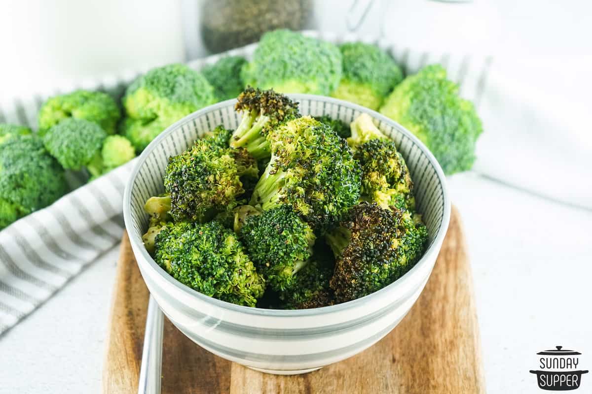 air fryer broccoli in a white bowl next to fresh broccoli florets, uncooked