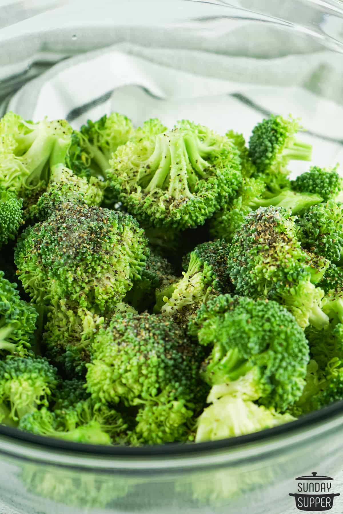 tossing broccoli with seasonings in a glass bowl