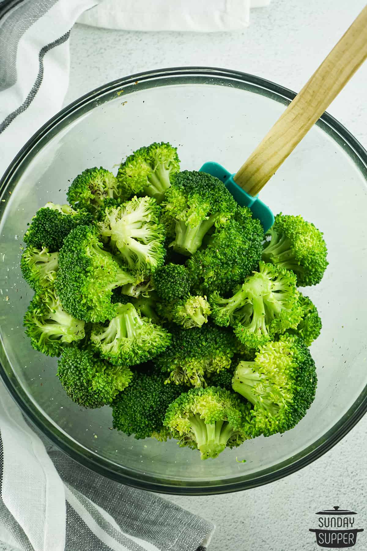mixing broccoli with oil in a glass bowl using a spatula