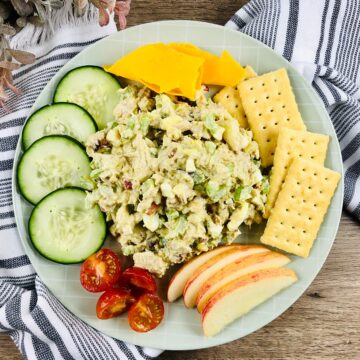 a closeup of a plate of tuna salad with crackers, cheese, apples, tomatoes, and cucumbers