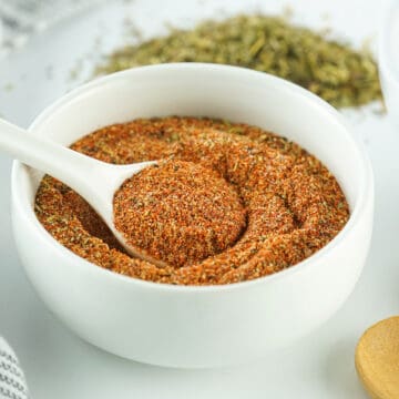 a white bowl of cajun seasoning with a small spoon