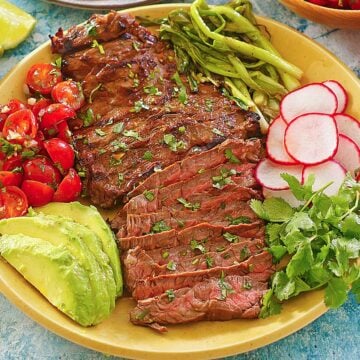 a plate of sliced carne asada and toppings