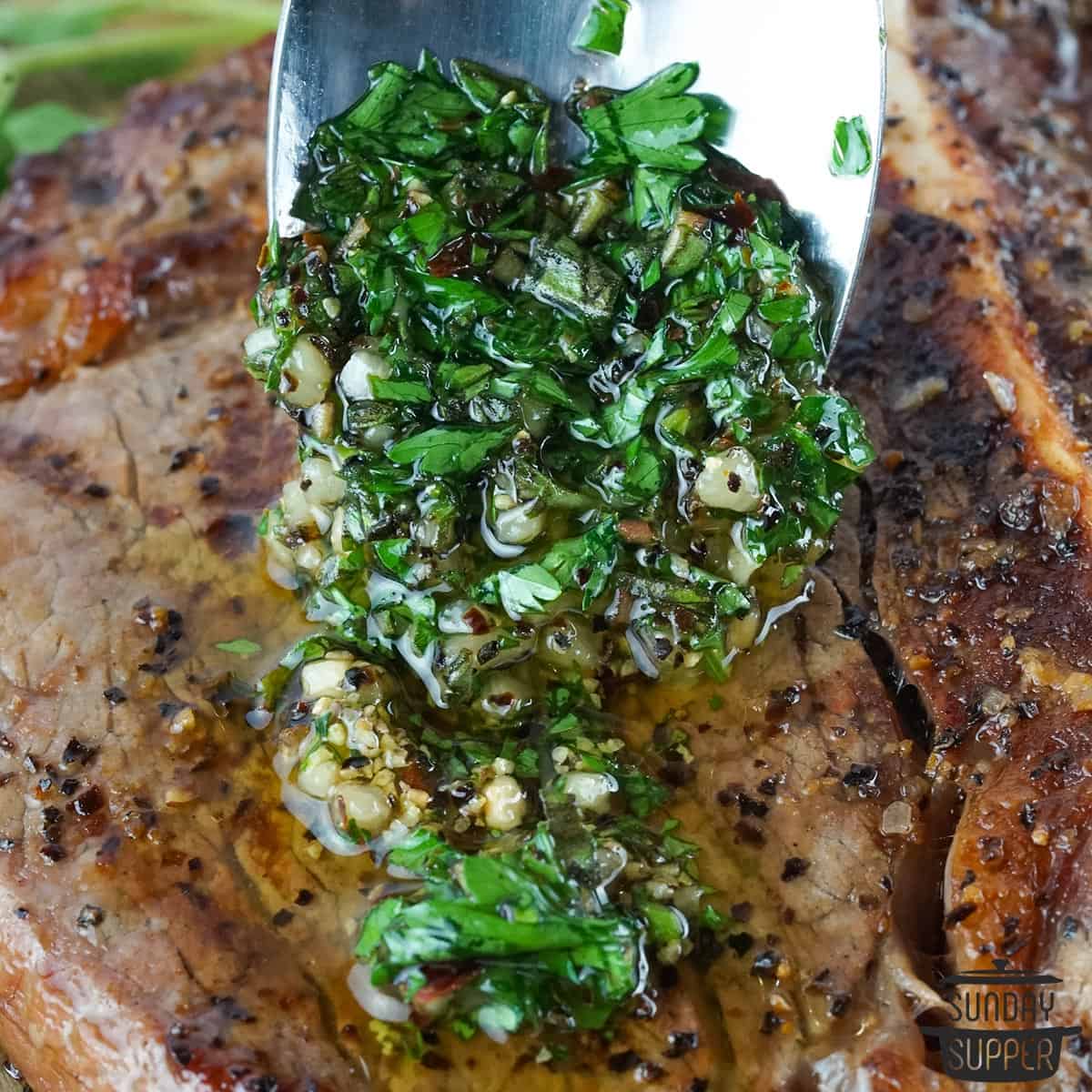 a spoon pouring chimichurri on to a steak