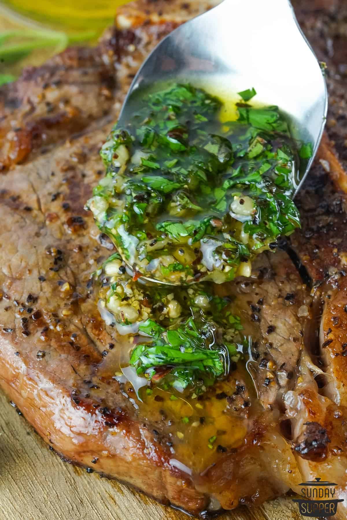 a spoon filled with chimichurri being added to a meal