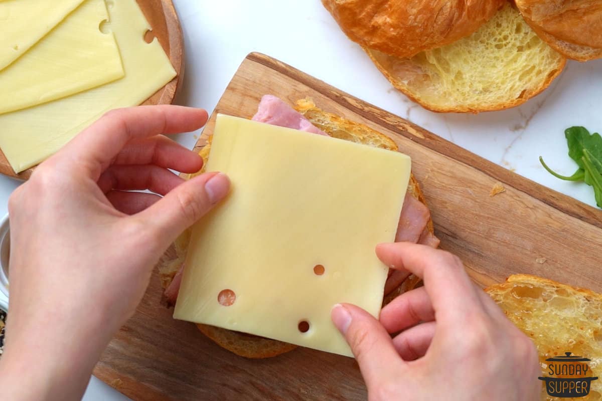 adding a slice of cheese to croissant