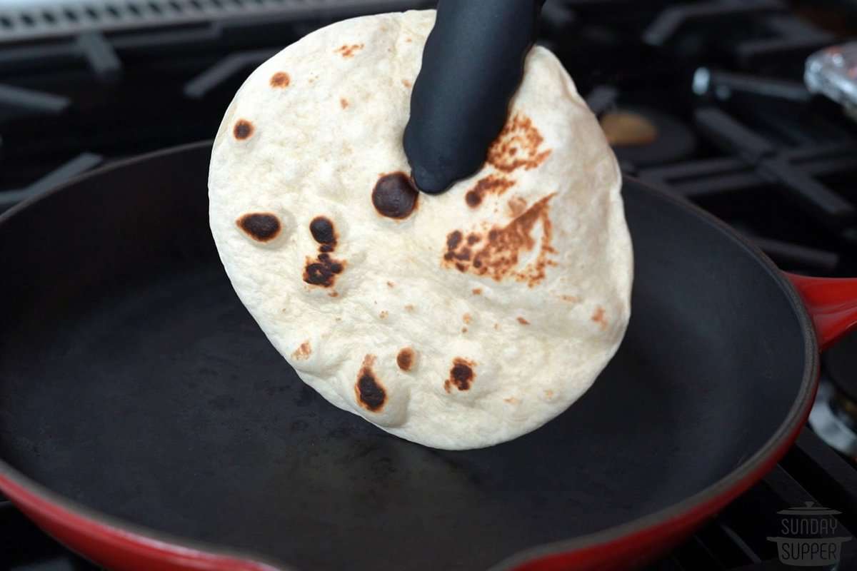 a tortilla being flipped on a pan with tongs