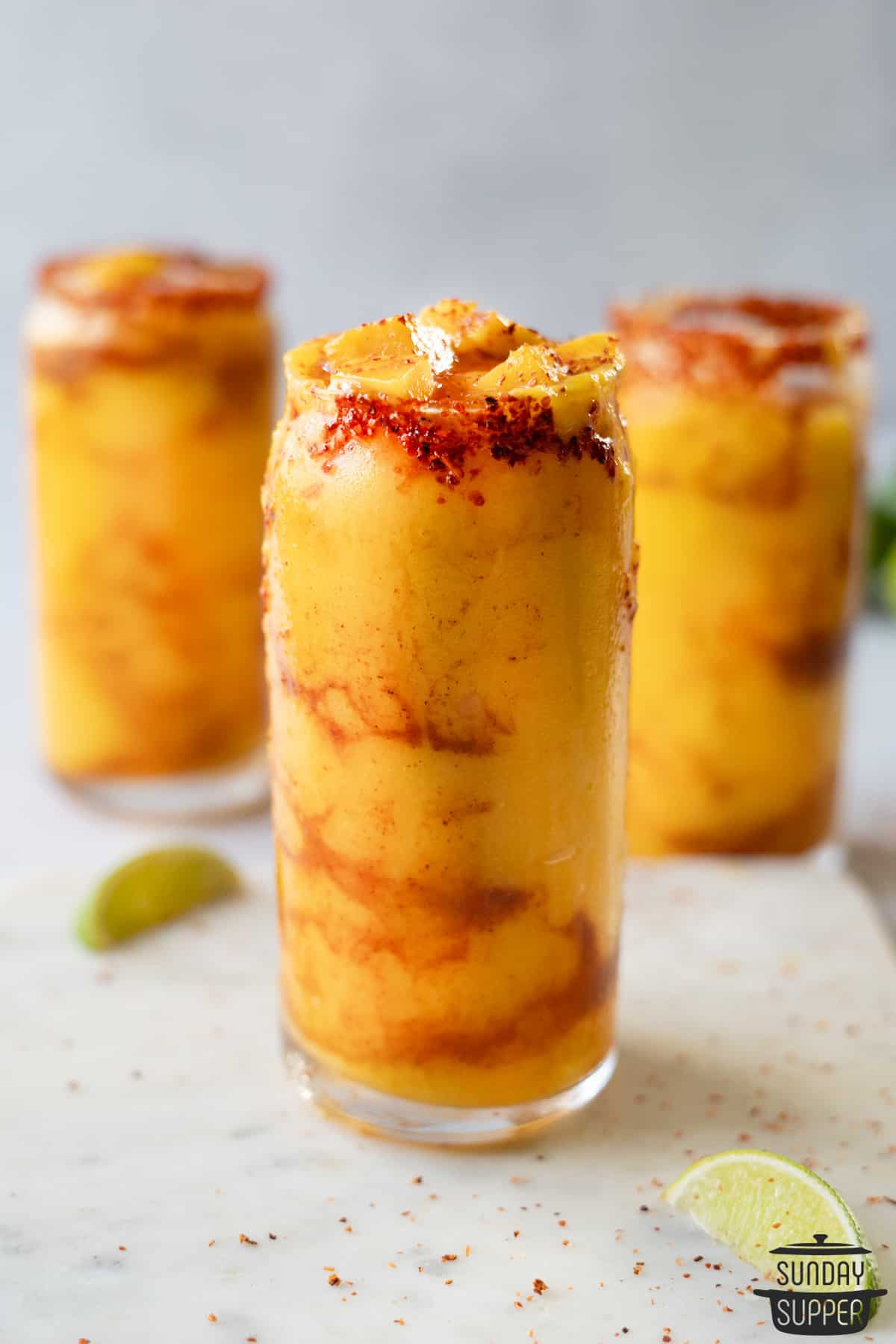 3 mangonadas in clear cups with fresh lime on the side