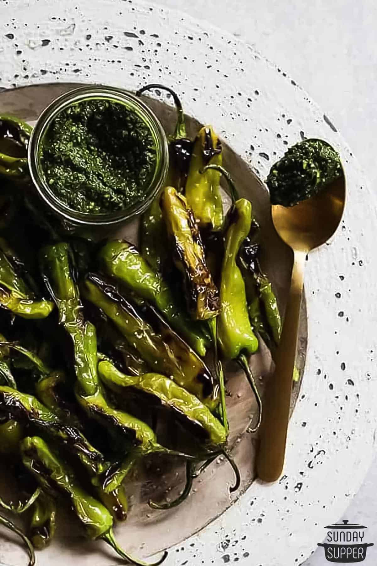 a plate of blistered peppers with a jar of pesto