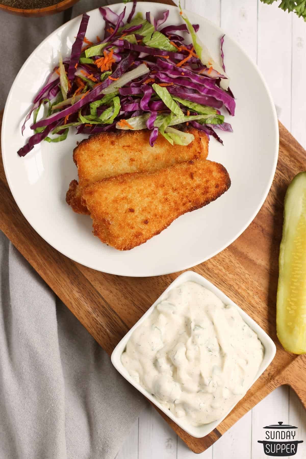a plate of fish fillets and cabbage slaw with tartar sauce
