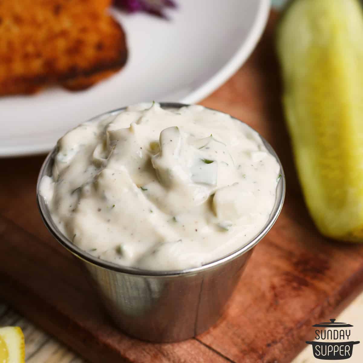 a metal dish of tartar sauce with dill pickles