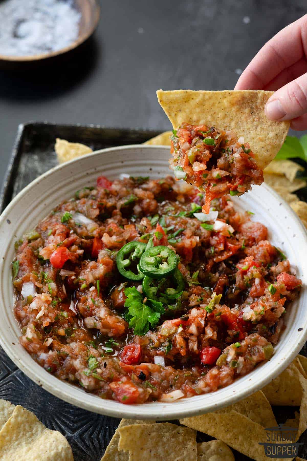 dipping a tortilla chip in tomato salsa