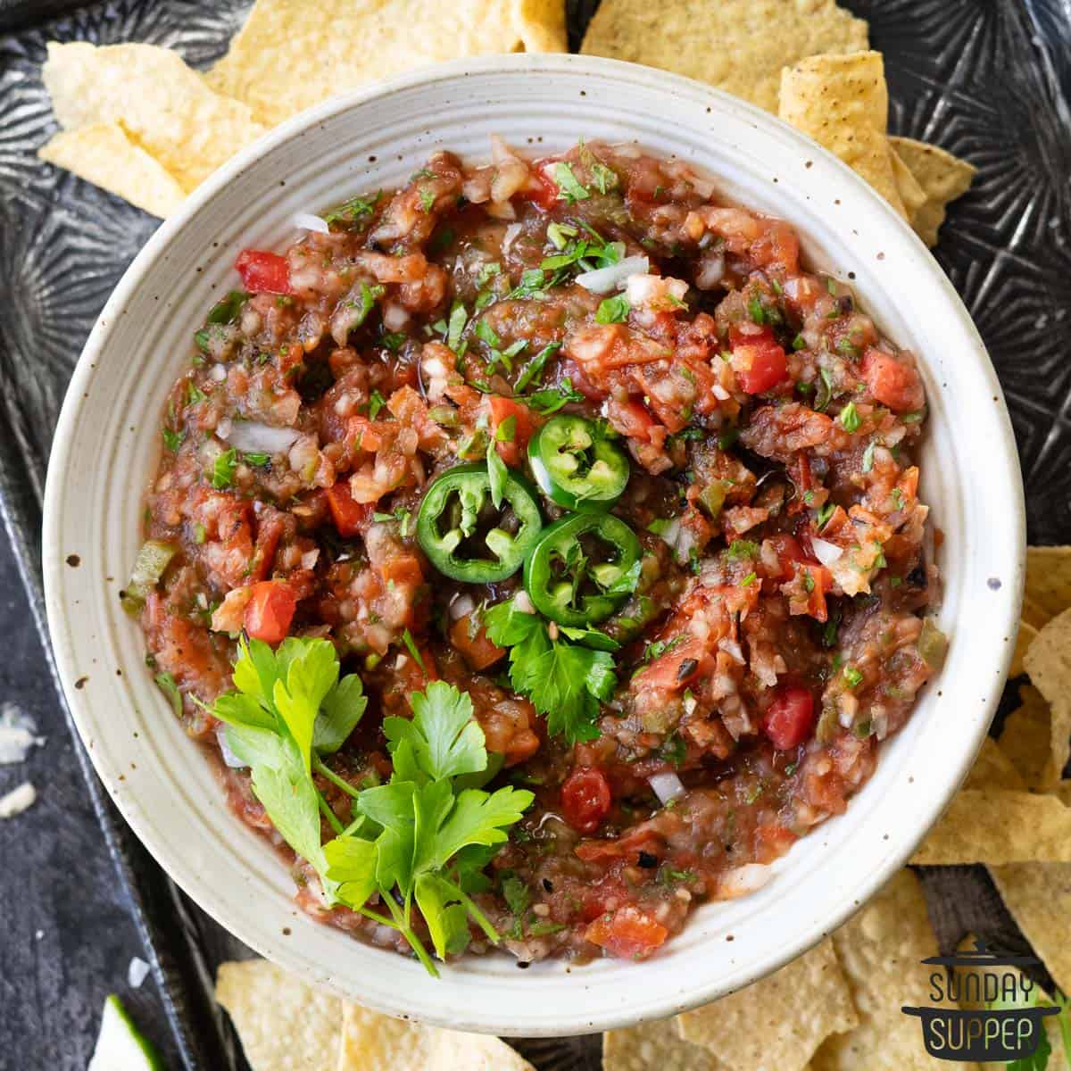 fresh tomato salsa in a bowl with cilantro, sliced jalapenos, and tortilla chips
