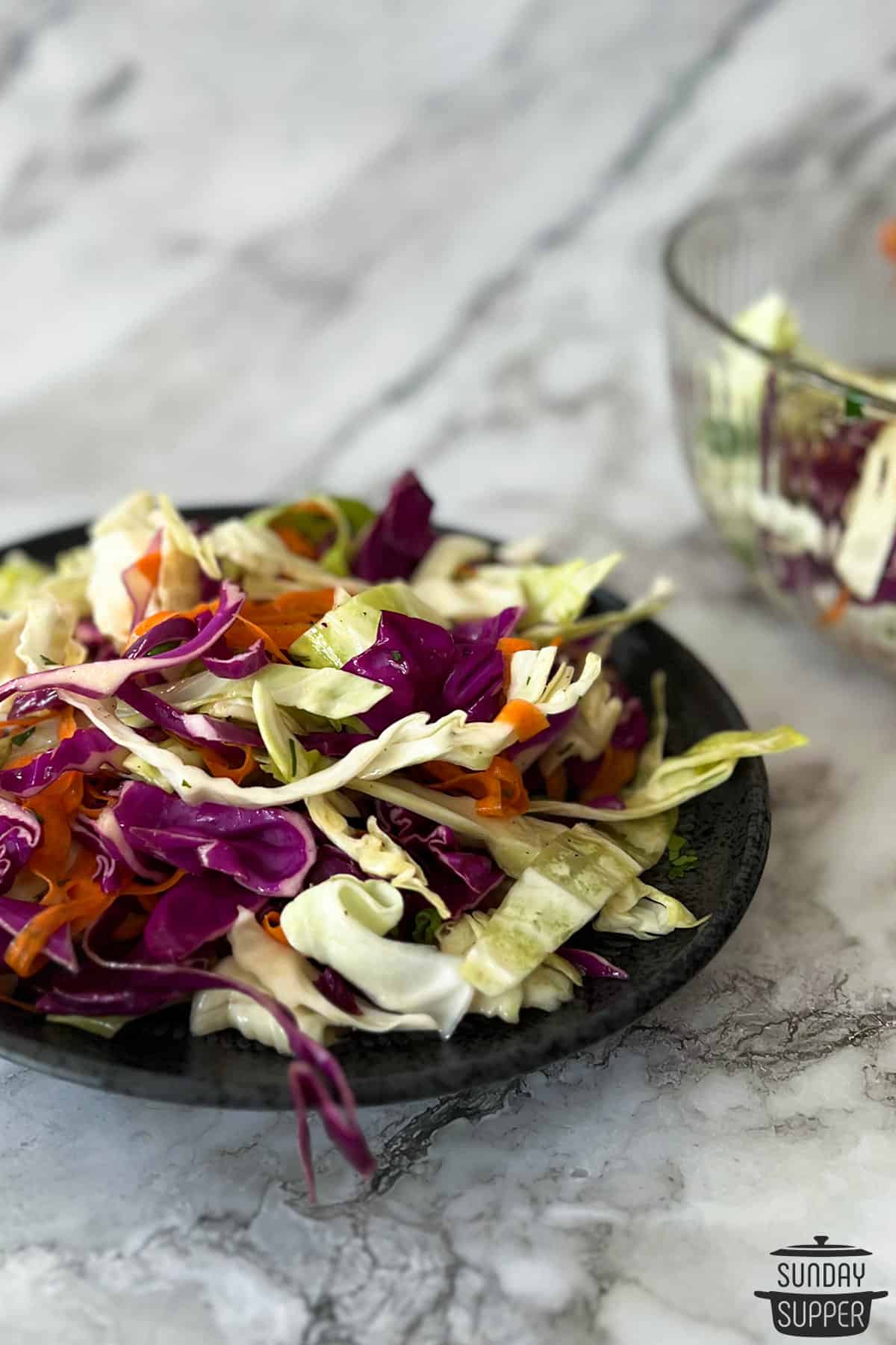 a plate of chinese coleslaw in front of a bowl of slaw
