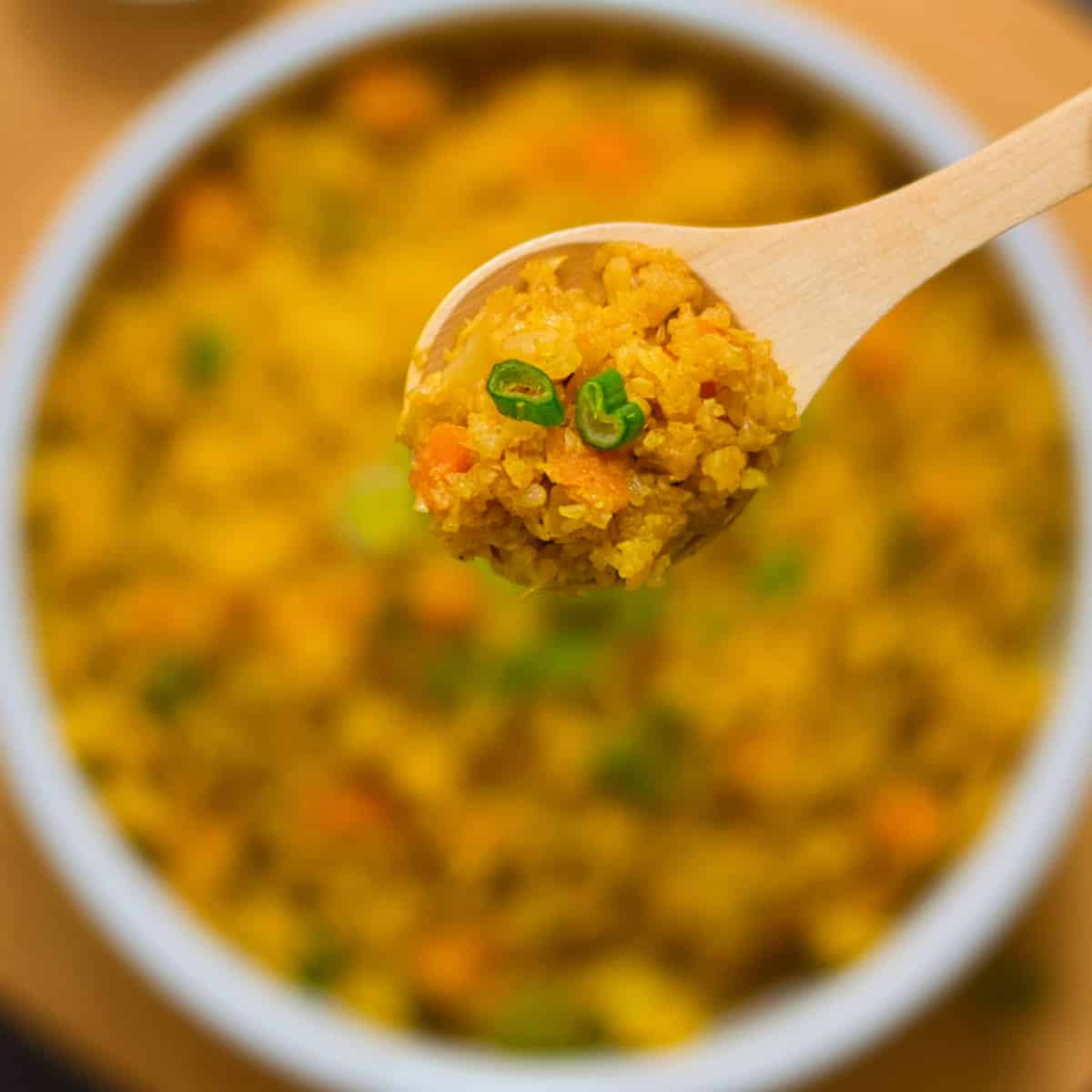 a wooden spoon of cauliflower rice over a bowl of rice