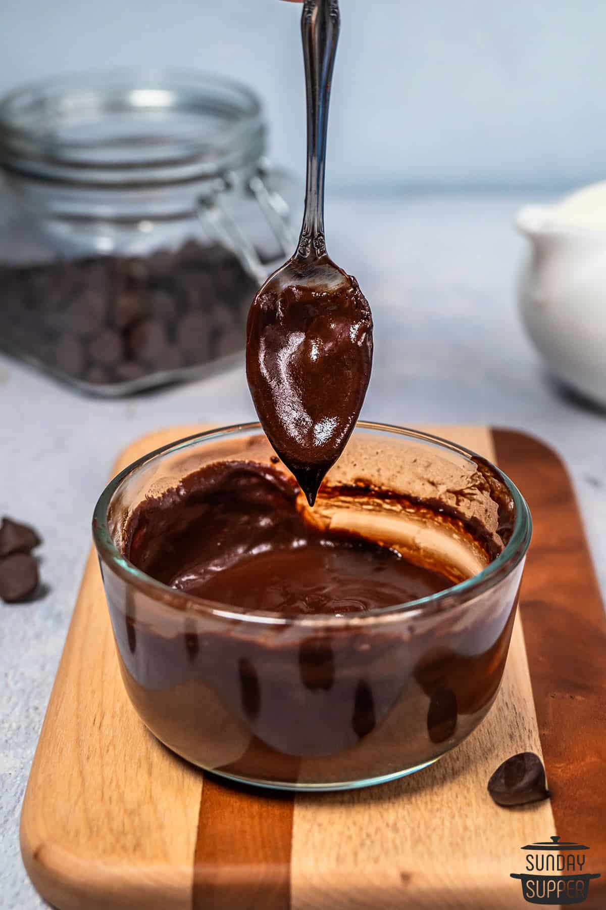 a spoon full of smooth and melted chocolate sauce in a dish