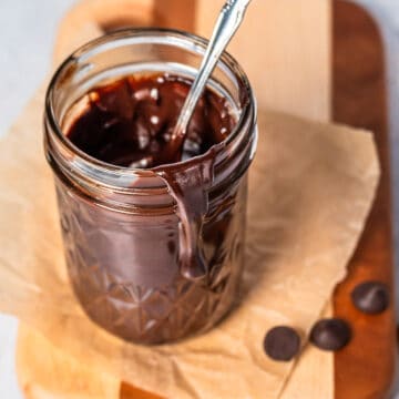 a glass jar of chocolate sauce on a cutting board with extra chocolate chips