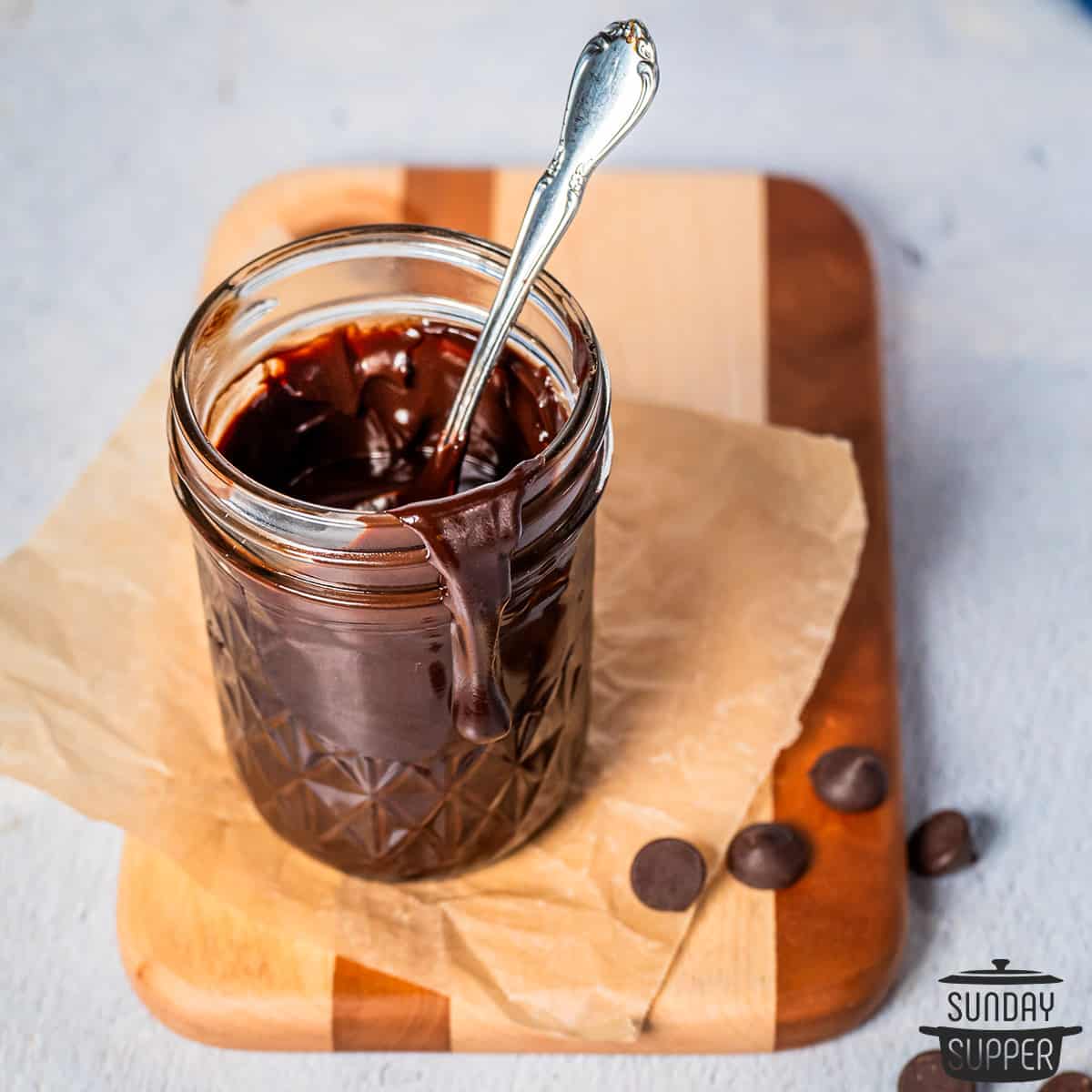 a mason jar filled with chocolate sauce on a cutting board with extra chocolate chips