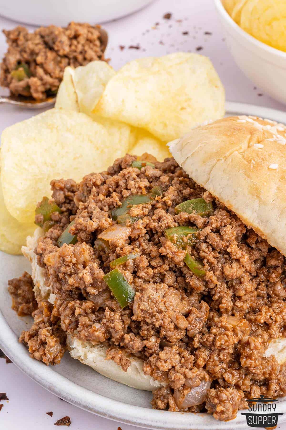 a bun piled with sloppy joe meat on a plate with chips