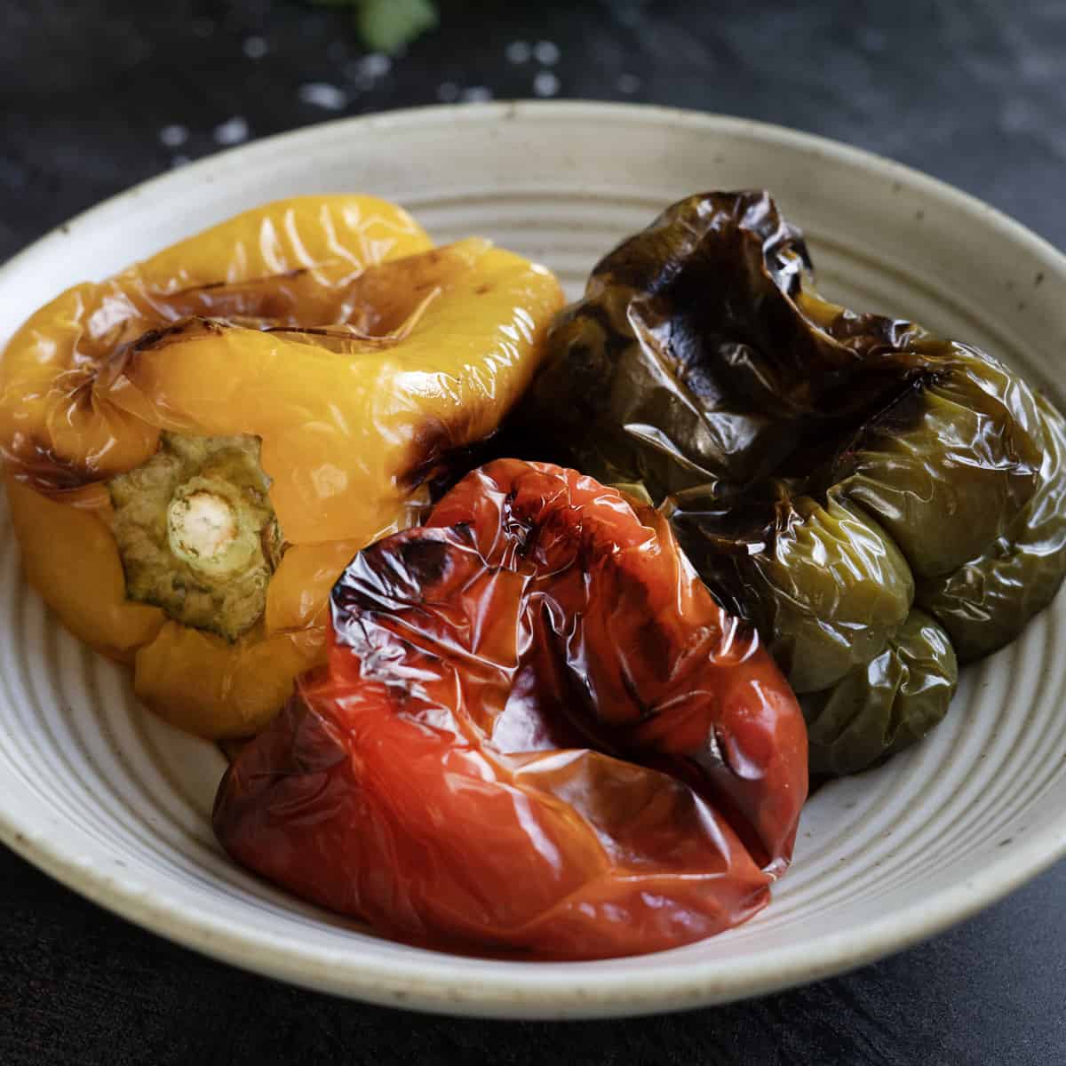 three roasted peppers on a plate before being peeled