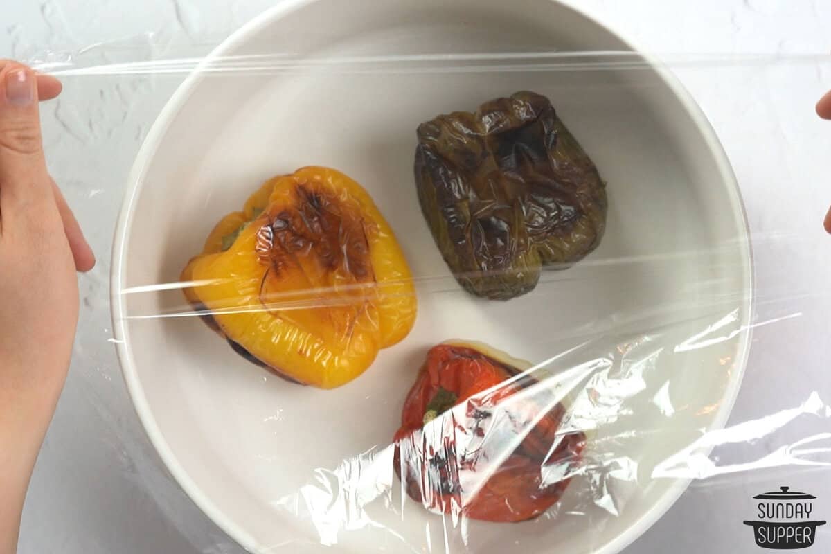 the roast peppers in a bowl with plastic over top