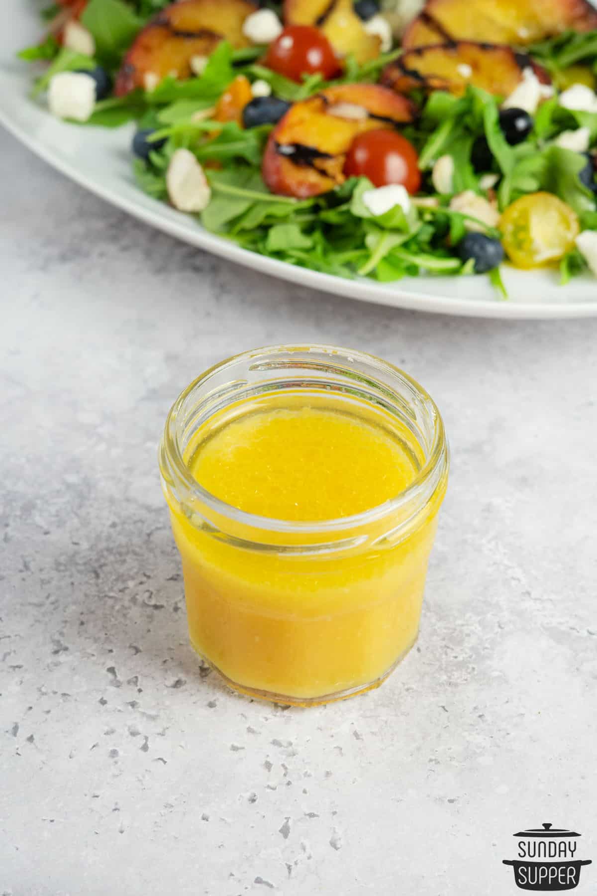 a jar of orange vinaigrette in front of a salad