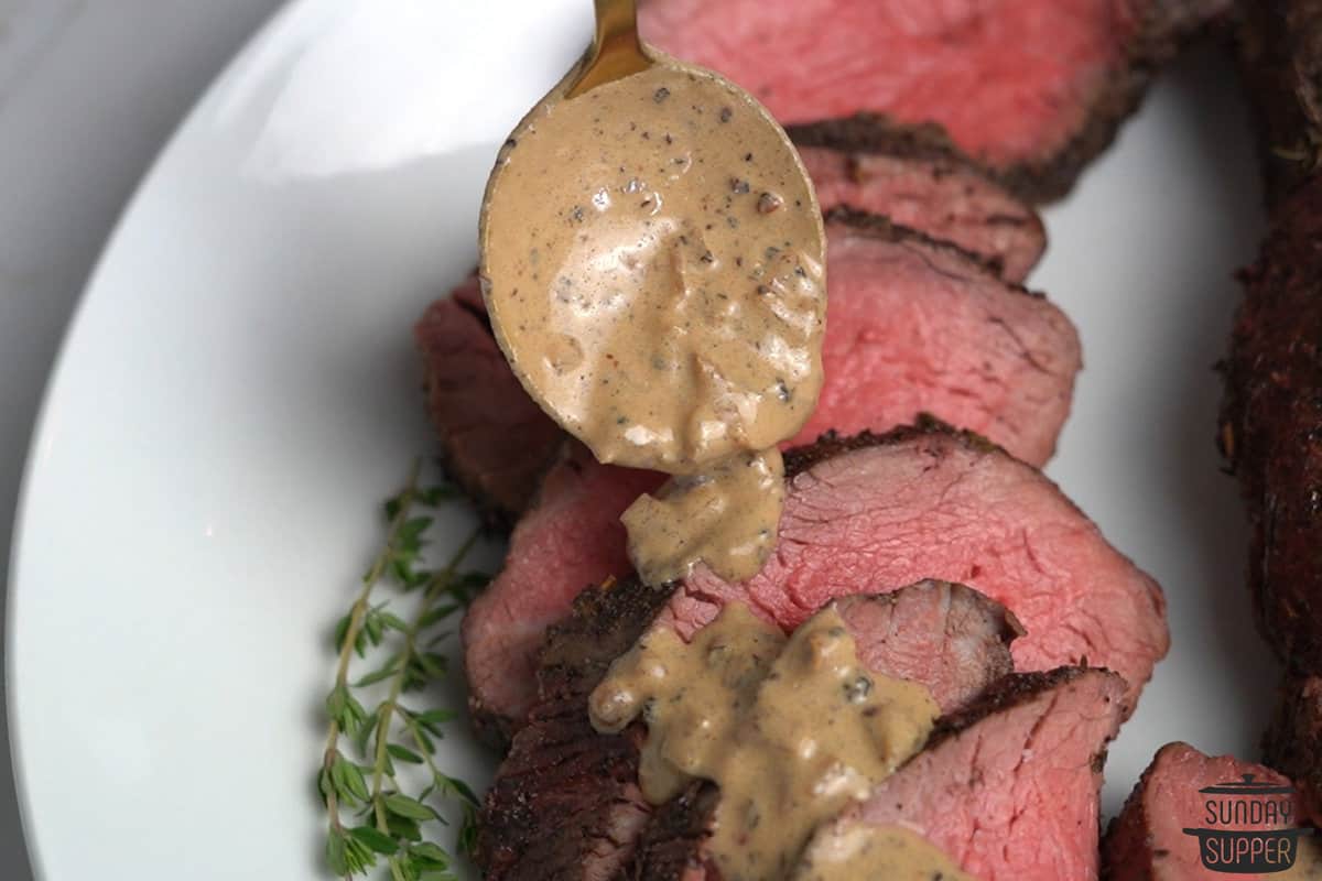 peppercorn sauce being poured over steak
