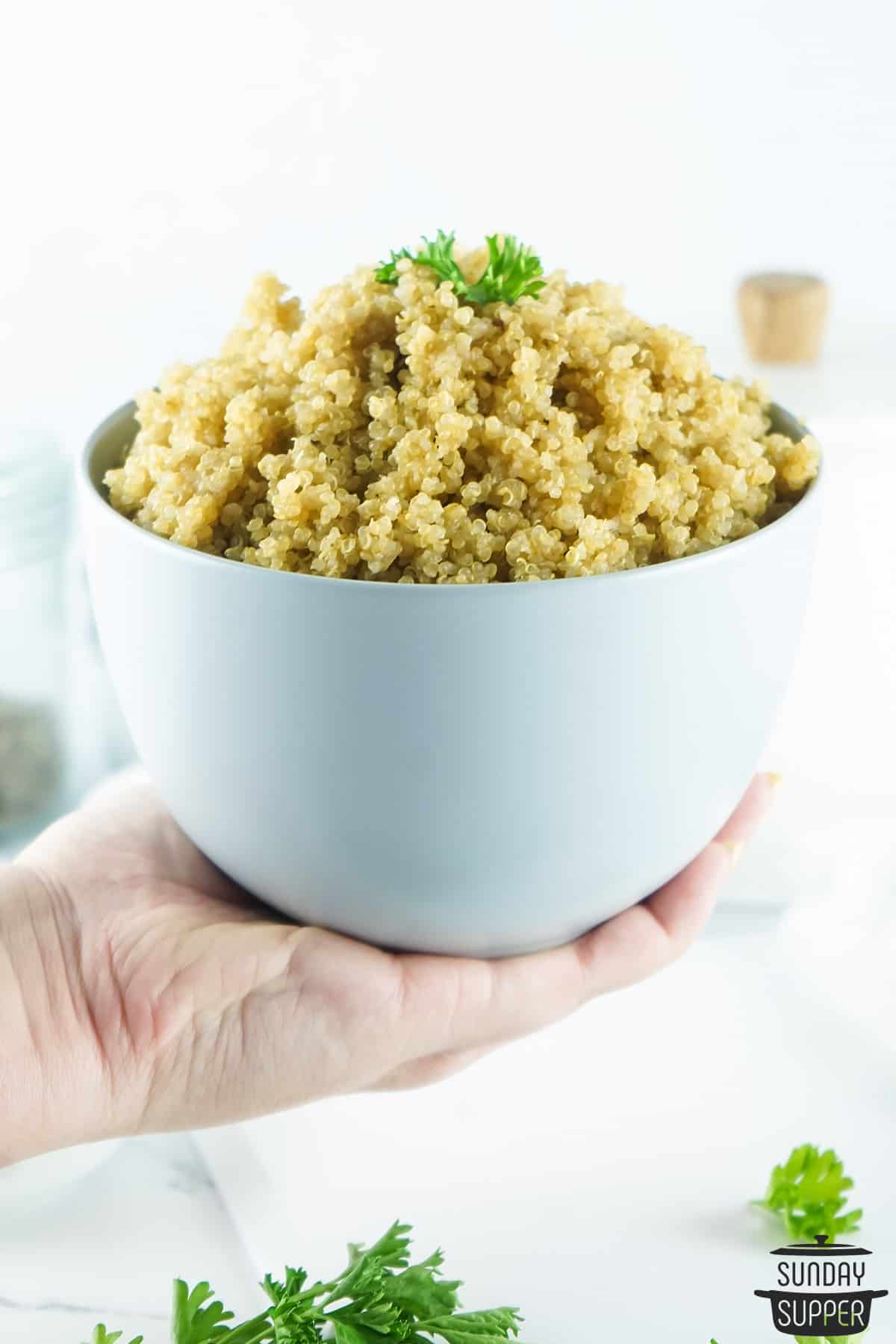 a hand holding a white bowl filled with cooked quinoa