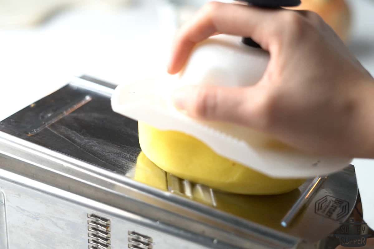 potatoes being sliced on a mandolin